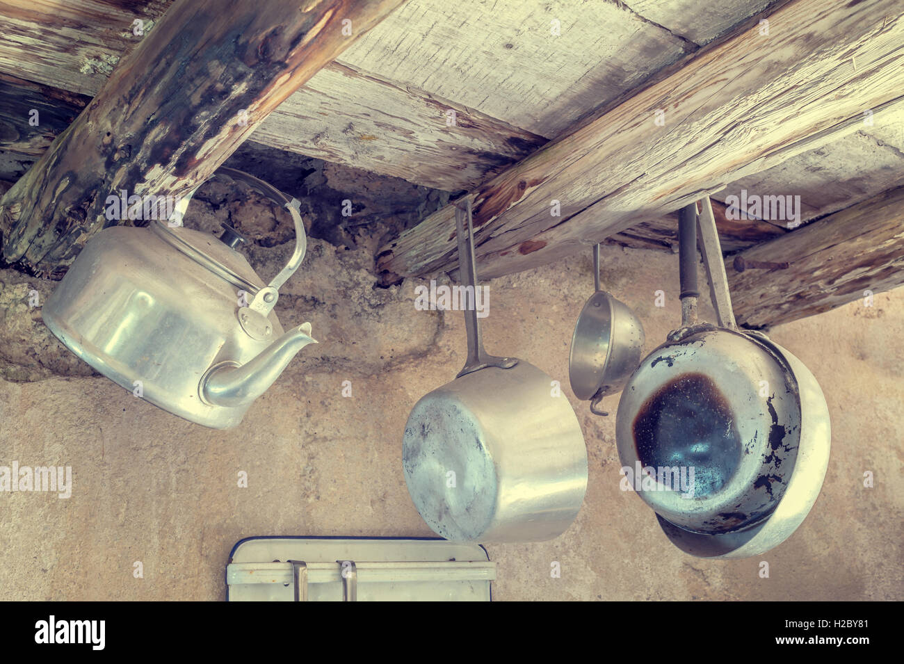 Alte Küchengeräte aus Aluminium. Von alten Holzbalken, Wasserkocher, Pfannen, Sieb hängen.  Foto in Vintage-Stile Stockfoto