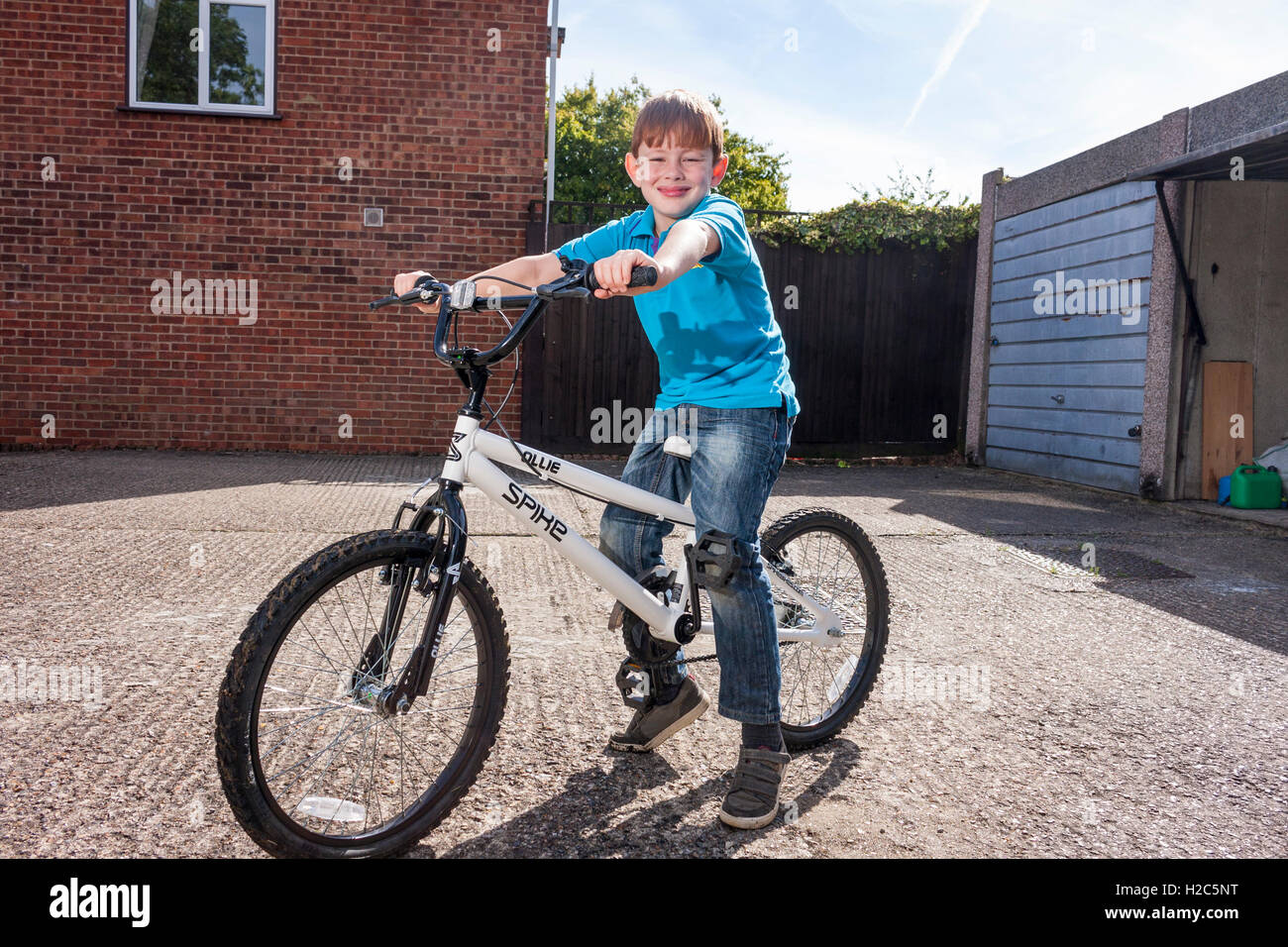 Ein kleiner Junge saß auf einem BMX Fahrrad außerhalb an einem sonnigen Tag ein helles Blau Biber Scout einheitliche t-Shirt Stockfoto