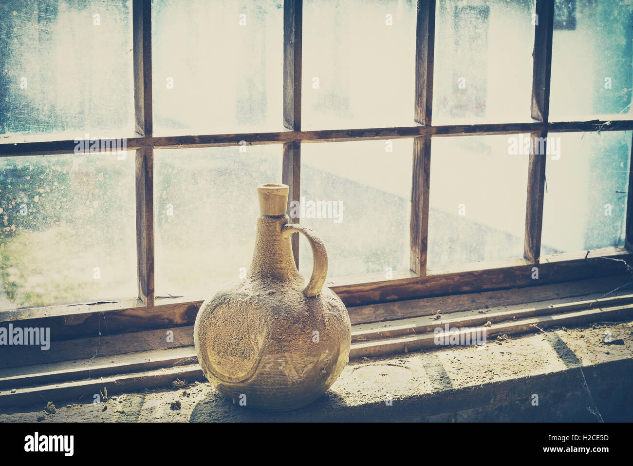 Retro gefiltert, eine alte verstaubte Ton Flasche durch ein Fenster. Stockfoto