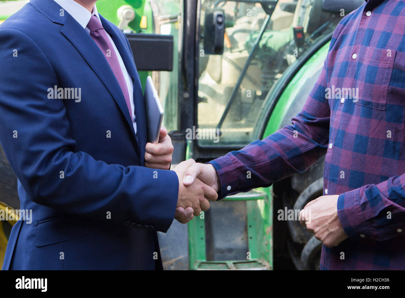 Landwirt und Geschäftsmann Händeschütteln mit Traktor im Hintergrund Stockfoto