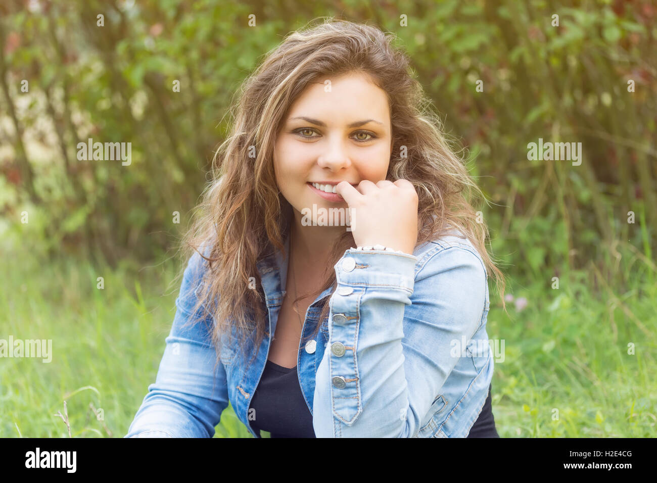 Porträt von verführerischen Lächeln auf den Lippen Teenager-Mädchen im Freien zu sitzen. Mädchen schaut die Kamera. Stockfoto