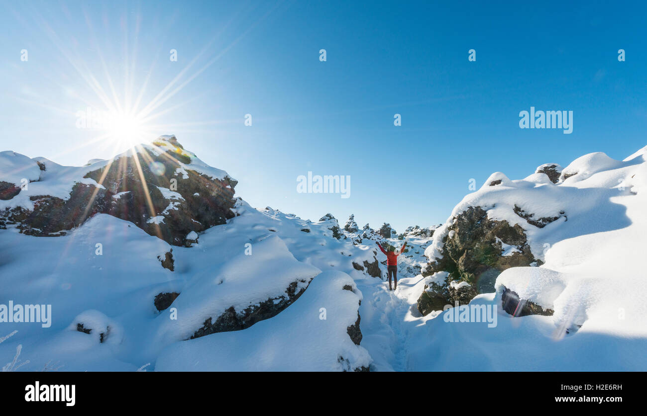 Frau mit Armen in der Luft, verschneite Landschaft mit Sonnenschein, Lavafeld bedeckt mit Schnee, Krafla Vulkansystem Stockfoto