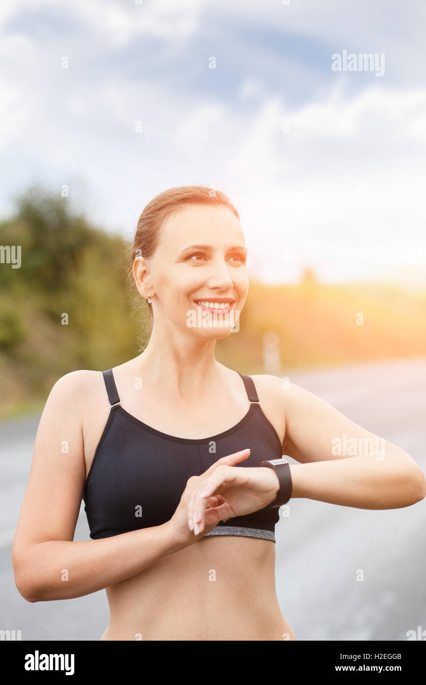 Junge, lächelnde Fitness Frau mit ihrem Smart watch für Herzfrequenz nach dem Joggen. Gesundes kaukasische Mädchen mit Fitness Tracker Armbanduhr Stockfoto