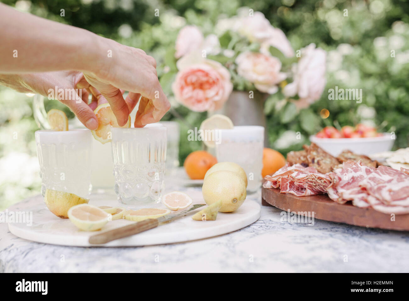 Nahaufnahme einer Frau, die Zubereitung, ein Holzbrett mit Aufschnitt auf einem Tisch in einem Garten. Stockfoto