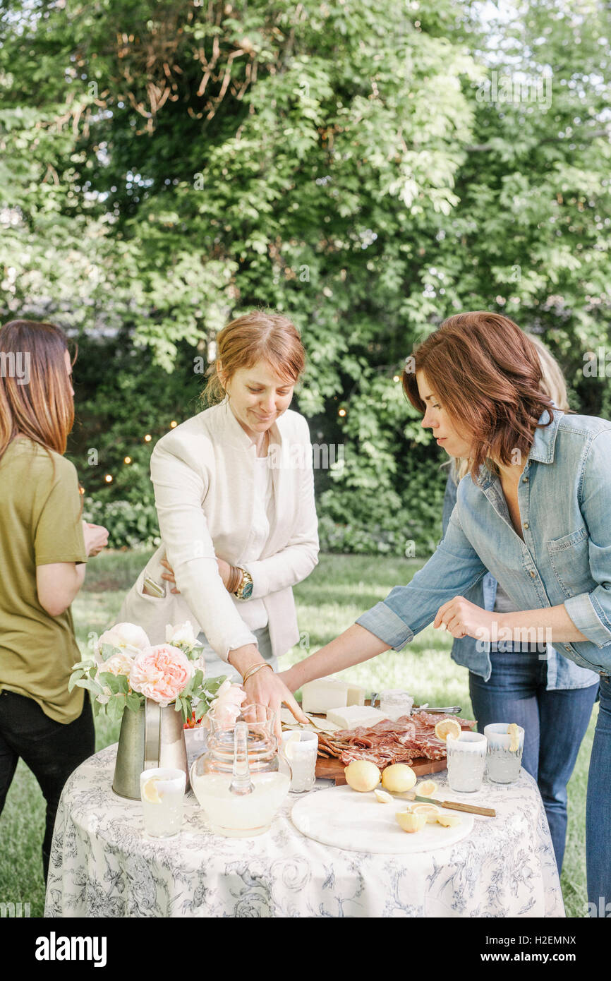 Drei Frauen stehen an einem Tisch mit Speisen und Getränken in einem Garten. Stockfoto