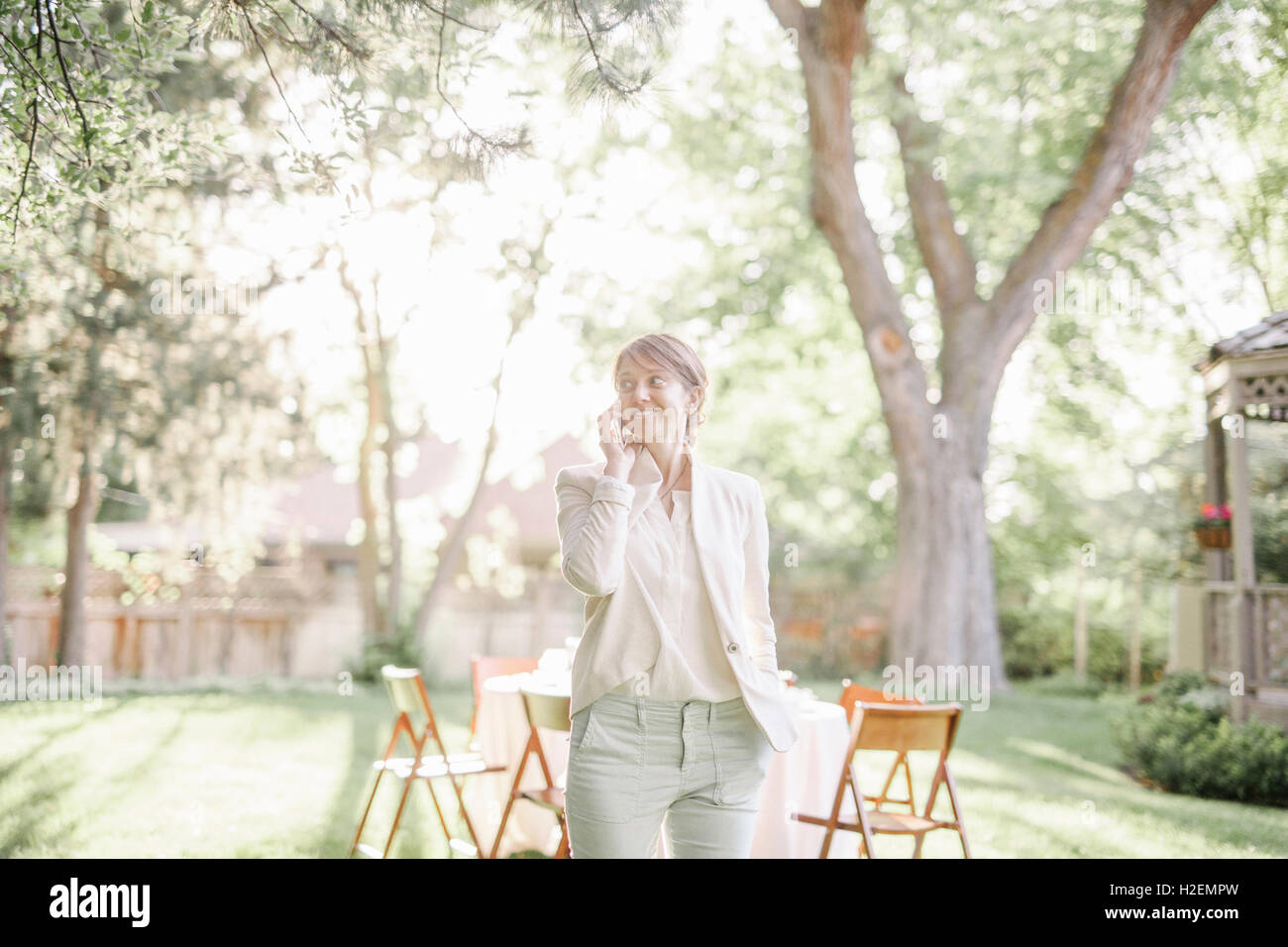 Frau stehend in einem sonnendurchfluteten Garten, telefonieren mit ihrem Handy. Stockfoto