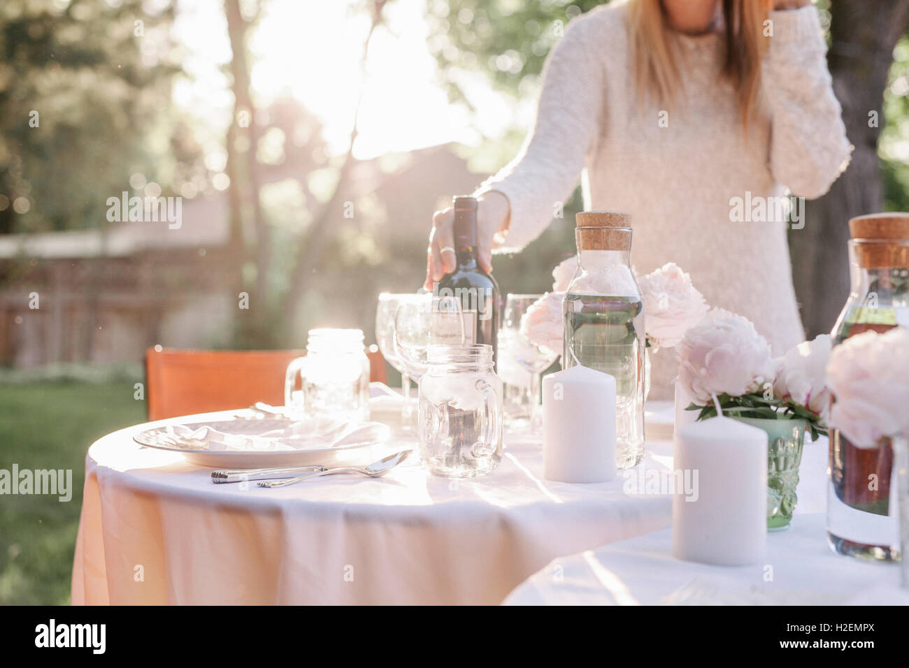 Frau einrichten einen Tisch in einem Garten, Kerzen und eine Vase mit rosa Rosen. Stockfoto