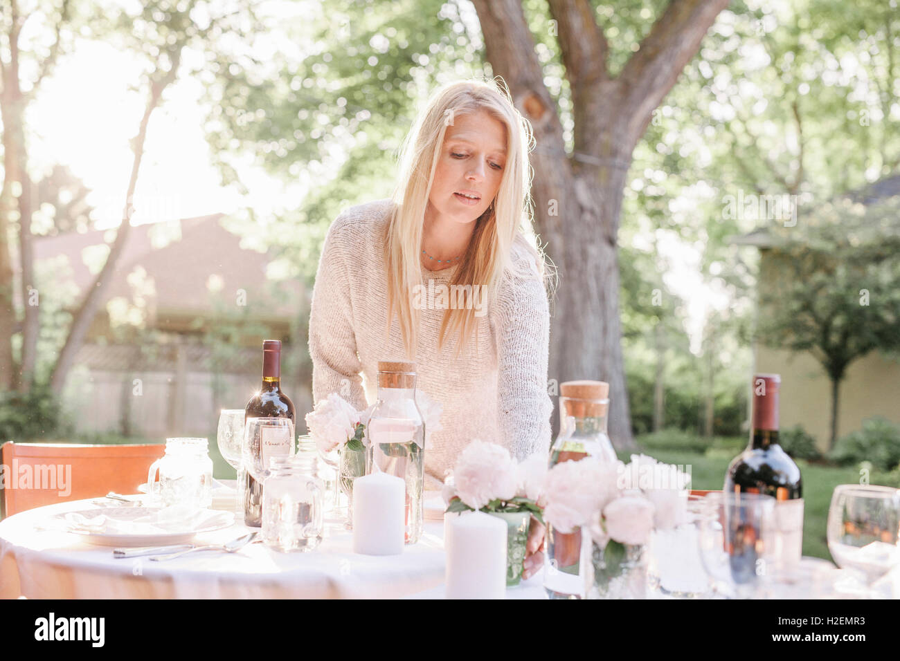 blonde Frau einrichten einen Tisch in einem Garten, Vasen mit rosa Rosen. Stockfoto