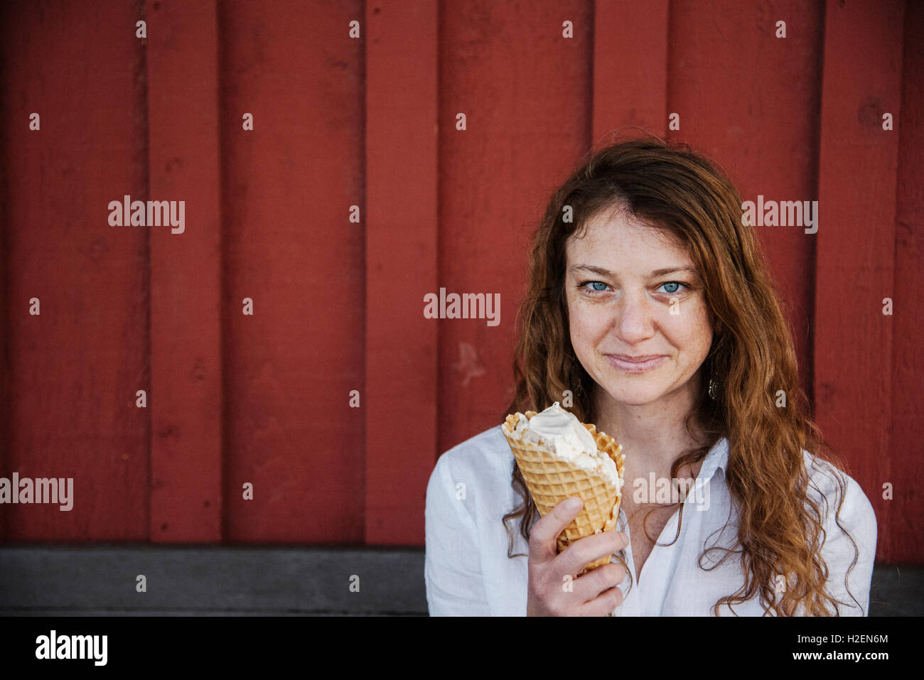 Frau mit Lon g braunen Haaren sitzen auf einer Bank, Eis essen. Stockfoto
