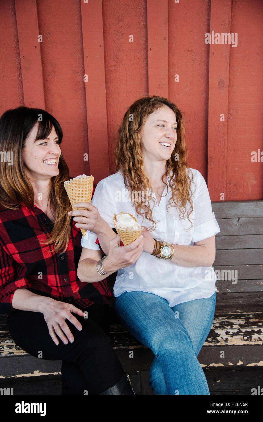 Zwei Frauen sitzen auf einer Bank, Eis essen. Stockfoto