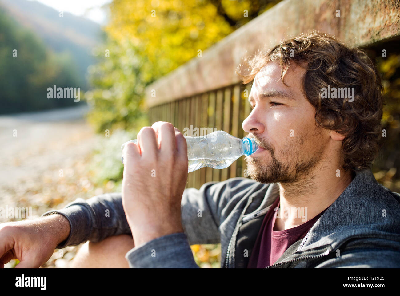 Junge hübsche Läufer mit Wasserflasche sitzen auf einer Brücke Stockfoto