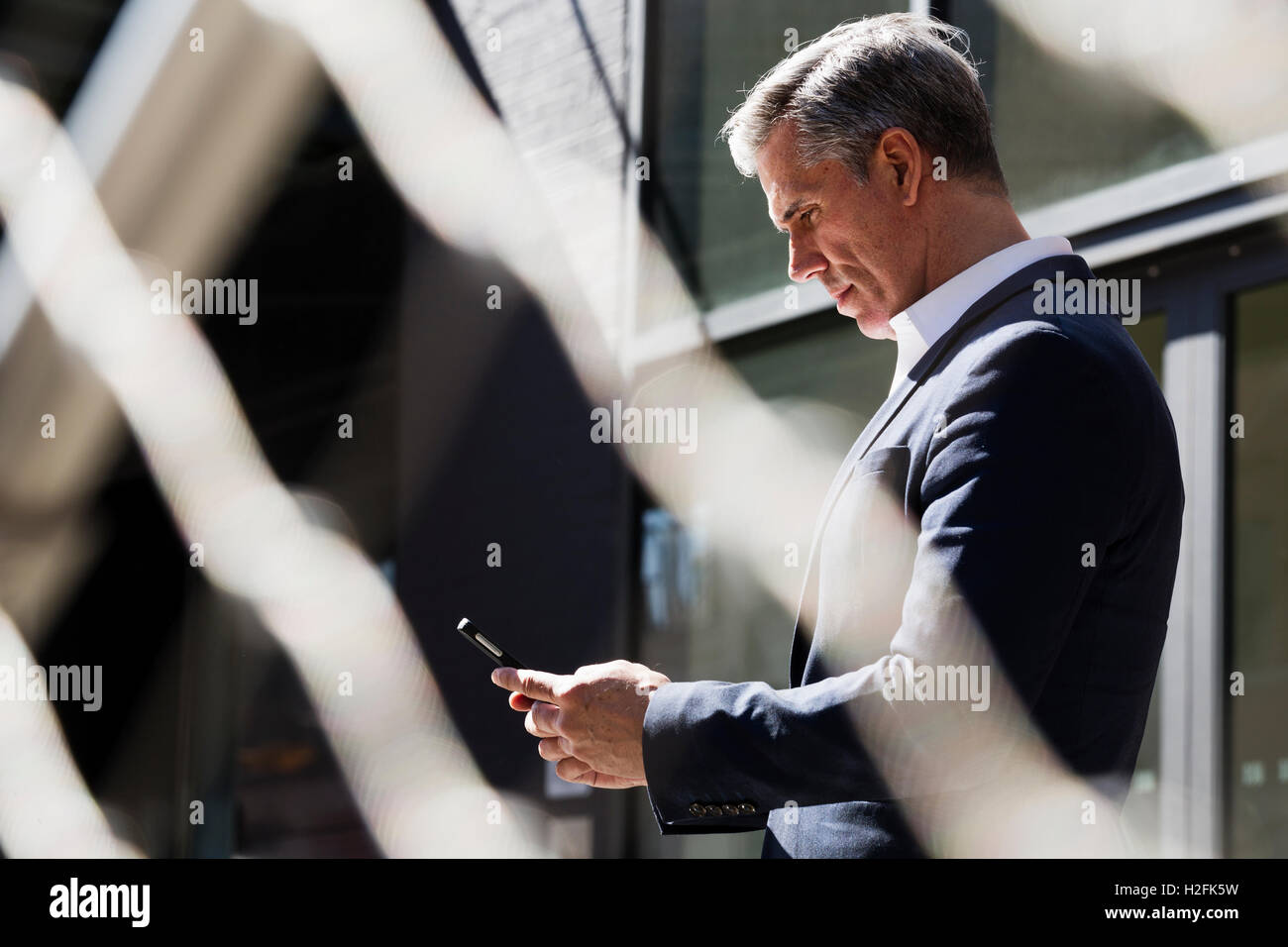 Ein Mann draußen unter einem Baum Überprüfung sein Telefon, Blick nach unten auf dem Bildschirm. Kommunikation für unterwegs. Stockfoto