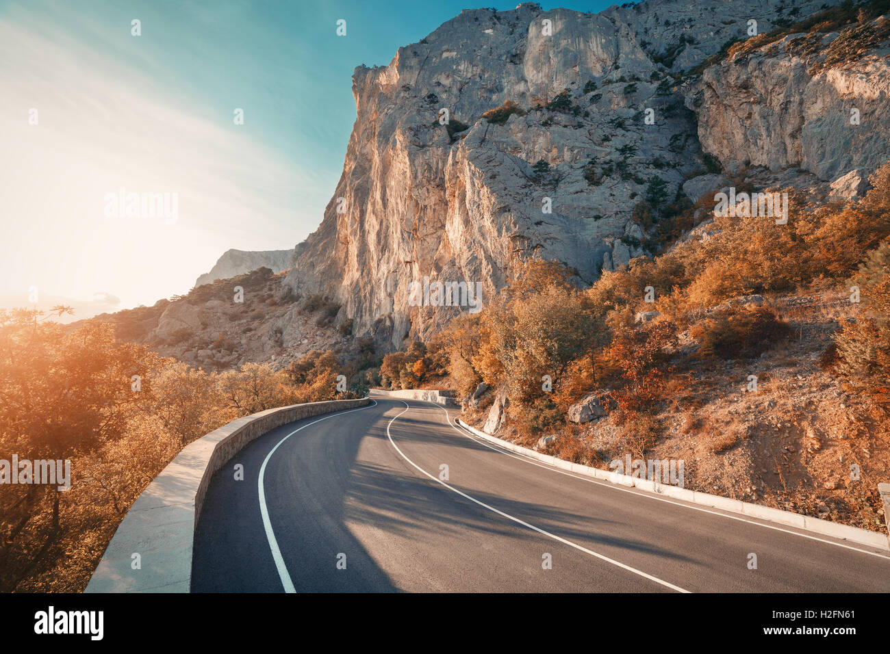 Asphaltierte Straße. Bunte Landschaft mit schönen Bergstraße mit perfekter Asphalt. Hohe Felsen, blaue Himmel bei Sonnenaufgang im Sommer. Stockfoto