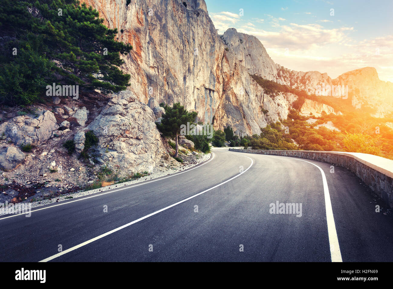 Schöne asphaltierte Straße. Bunte Landschaft mit hohen Felsen, Bergstraße mit perfekter Asphalt, Bäume, blauer Himmel bei Sonnenuntergang in s Stockfoto