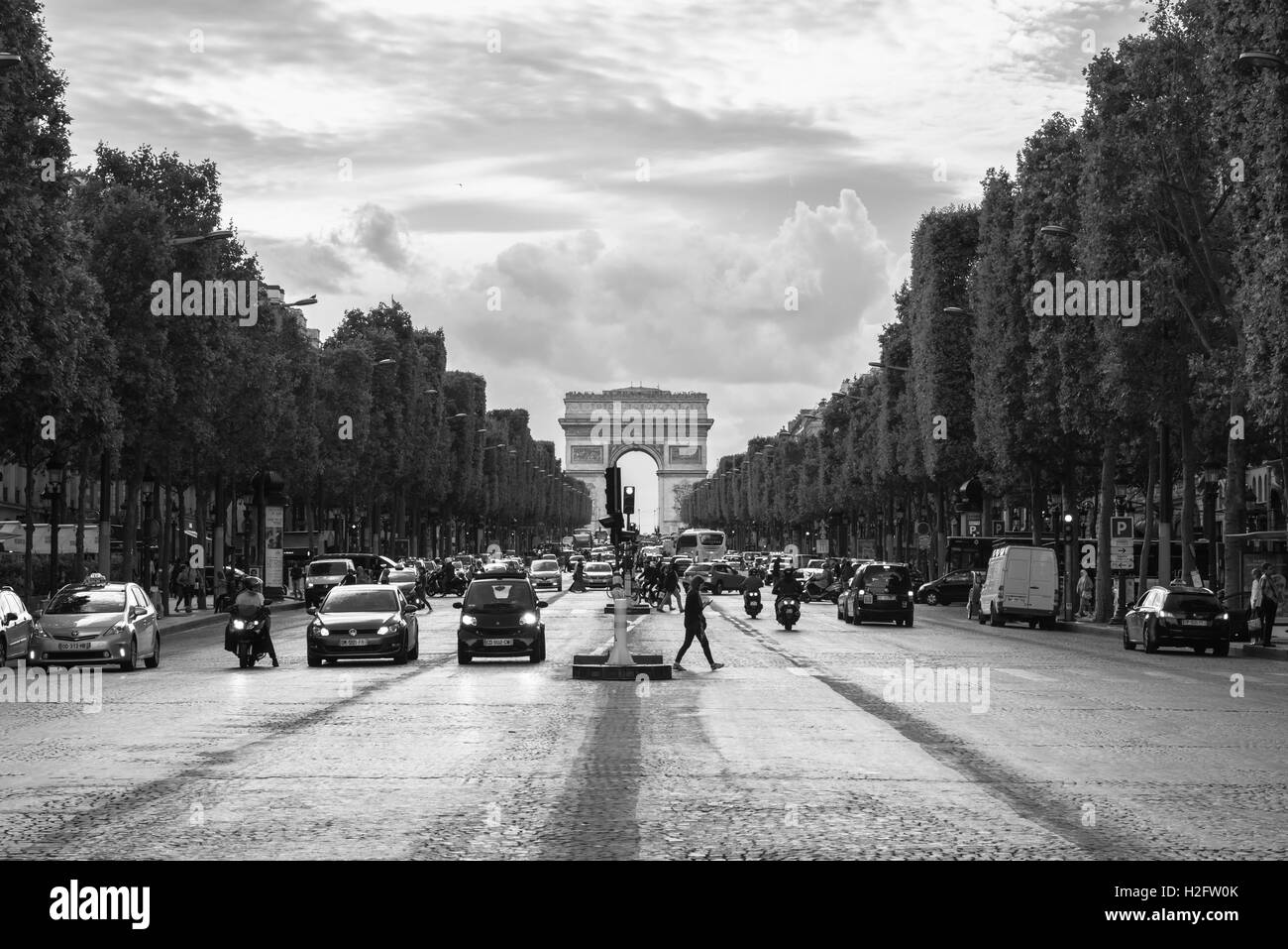 Eine Frau kreuzt die Champs-Elysees in Paris, Frankreich, mit der Arc De Triomphe de l'Étoile im Hintergrund zu sehen. Stockfoto