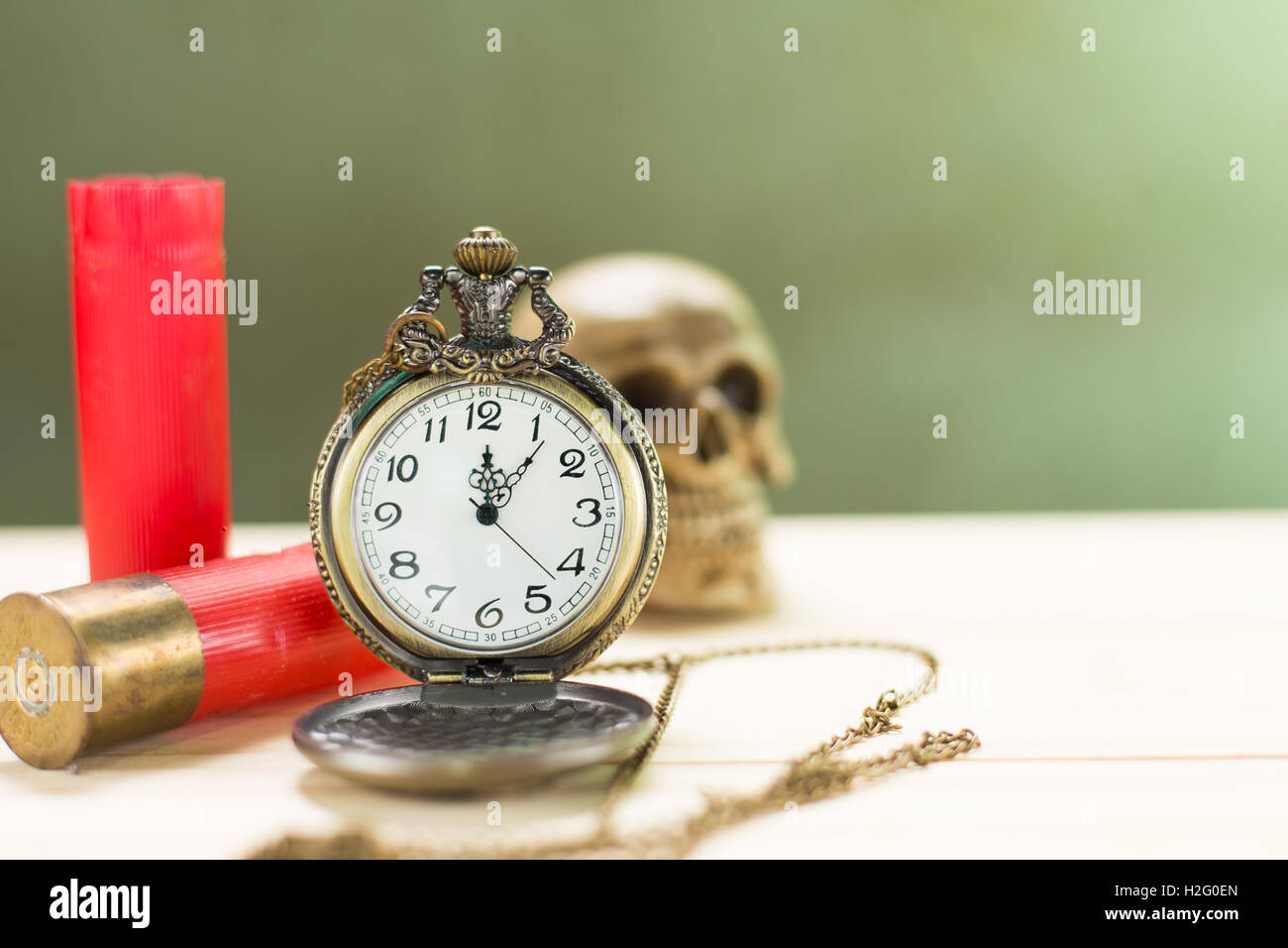 Stilleben Antike Uhr auf einen Holzboden und eine rote Shotgun Shell mit menschlichen Schädel auf dem Hintergrund platziert. Stockfoto
