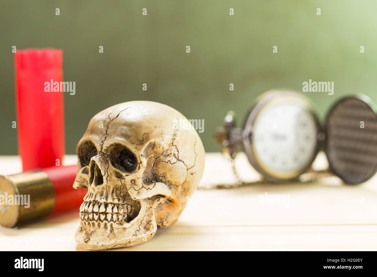 Menschlicher Schädel ruht auf einem Holzfußboden und einer roten Schrotflinte Shell mit antiken Uhren im Hintergrund. Stockfoto