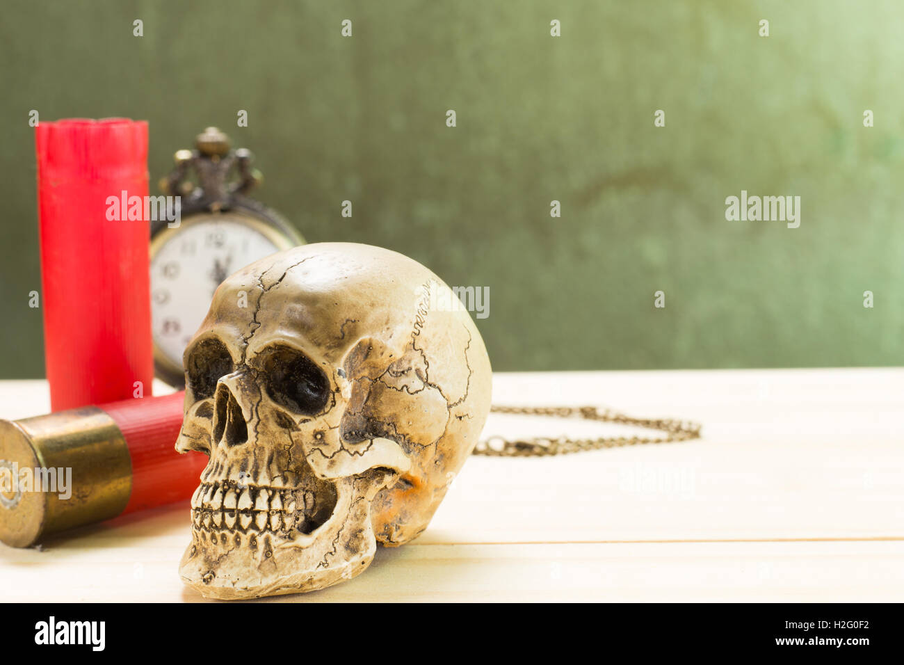 Menschlicher Schädel ruht auf einem Holzfußboden und einer roten Schrotflinte Shell mit antiken Uhren im Hintergrund. Stockfoto