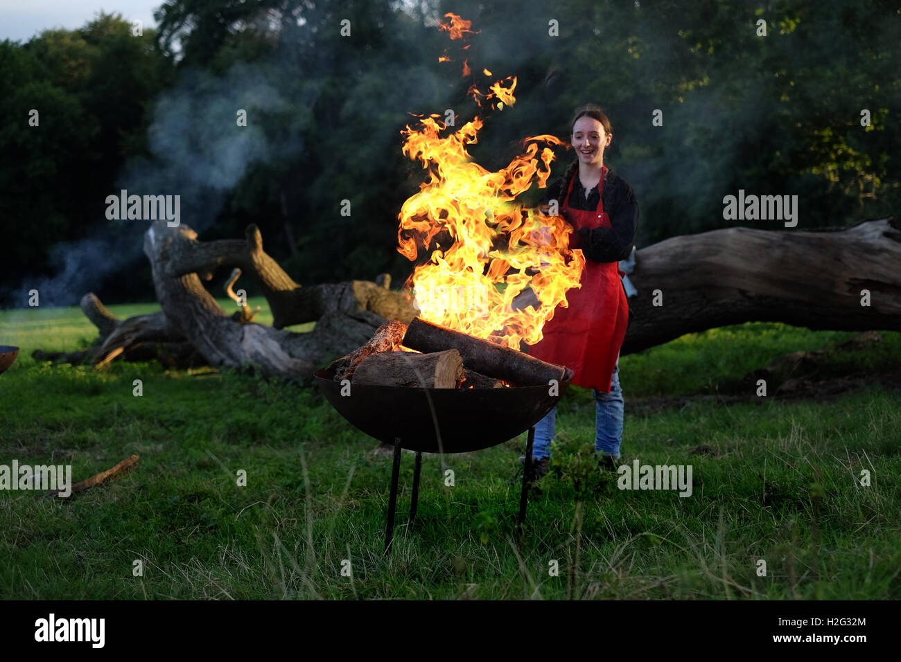 Eine Frau neigt dazu, das Feuer in der roten Erde Event, Genius Loci, knackige Flammen flackern vor ihr Gesicht. Stockfoto