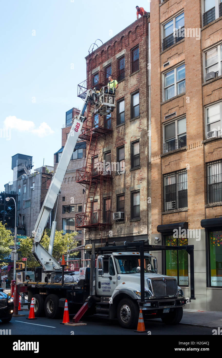 Männer, die aus einer Hubarbeitsbühne arbeiten, das Dach von einem alten Mietshaus in Soho in New York City reparieren Stockfoto