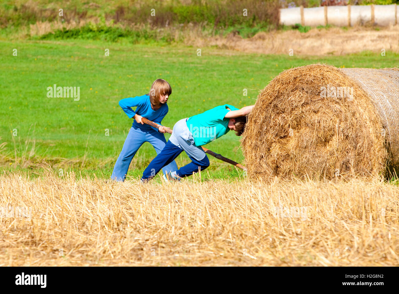 Zwei jungen, die Ballen Heu mit Stick als Hebel bewegen Stockfoto