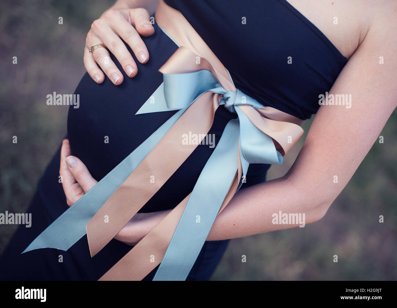 Schwangere Frau hält Hände einen Magen mit Bogen Stockfoto