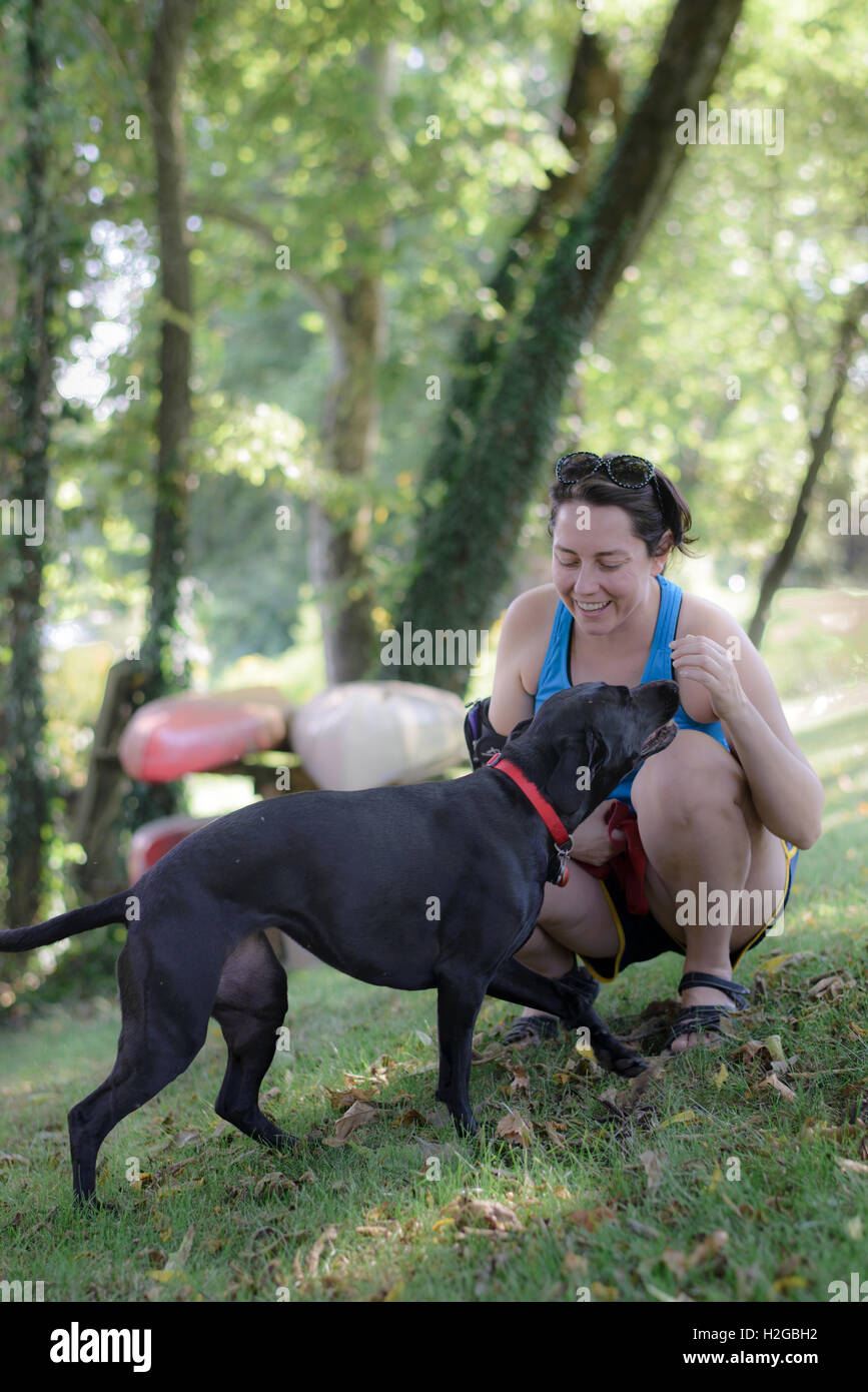 Frau in einem holzigen schattigen Ort mit ihrem Hund und Kanus im Hintergrund Stockfoto