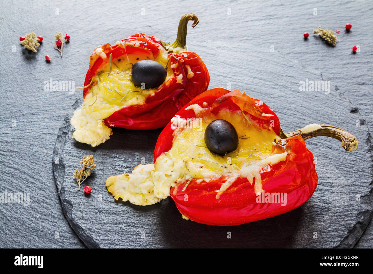 Gefüllte rote Paprika mit Feta-Käse und Oliven auf schwarzem Stein. Stockfoto