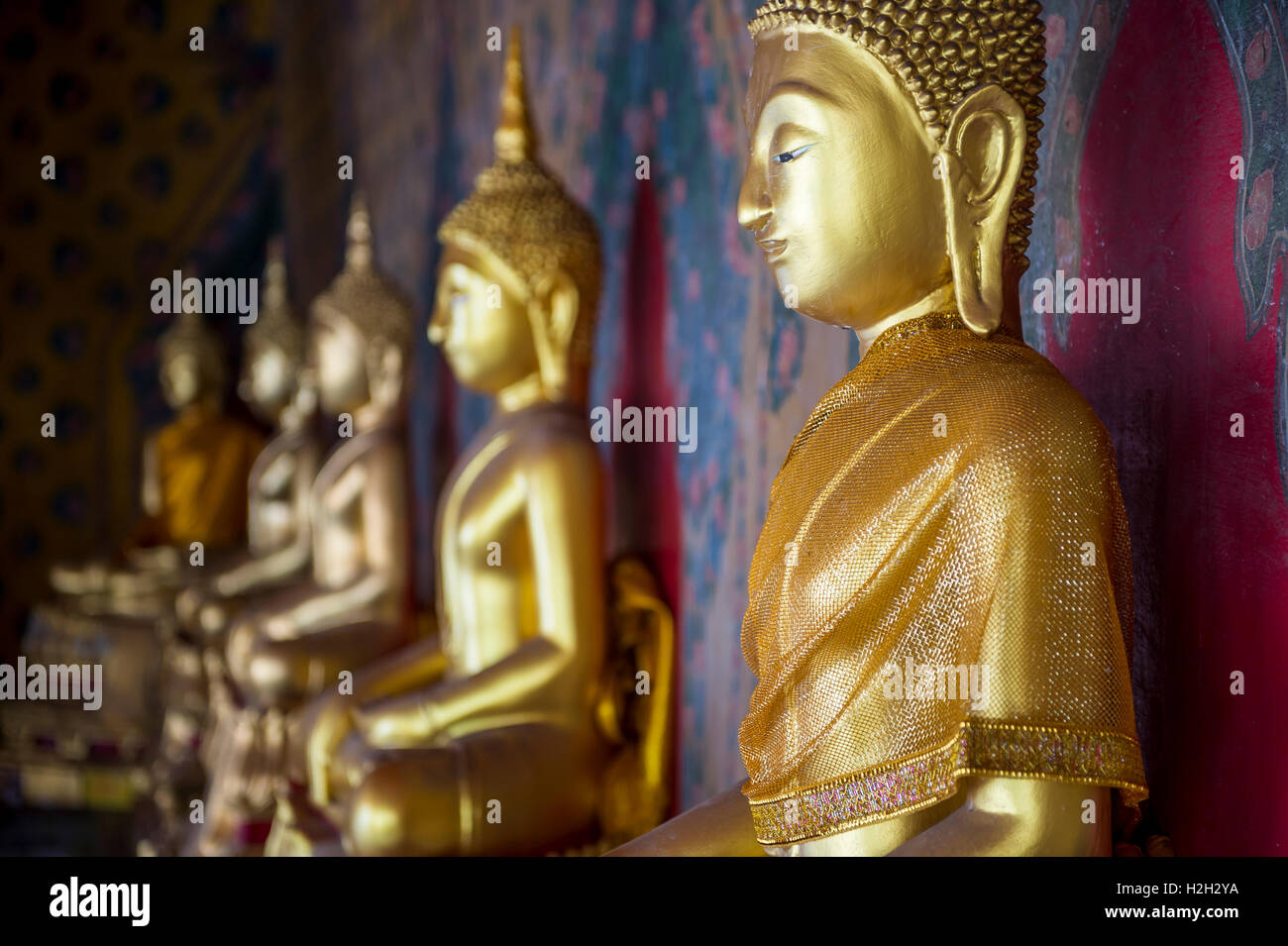 Reihe von Golden sitzenden Buddhas tragen gelbe Schärpe vor dekorative Wand in einem buddhistischen Tempel in Bangkok Thailand Stockfoto