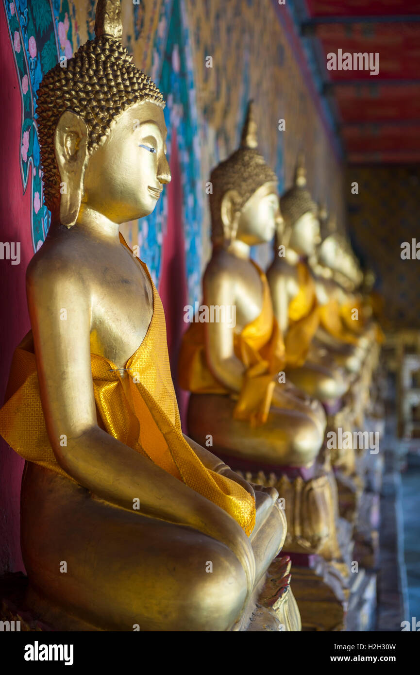 Reihe von Golden sitzenden Buddhas tragen gelbe Schärpe vor dekorative Wand in einem buddhistischen Tempel in Bangkok Thailand Stockfoto