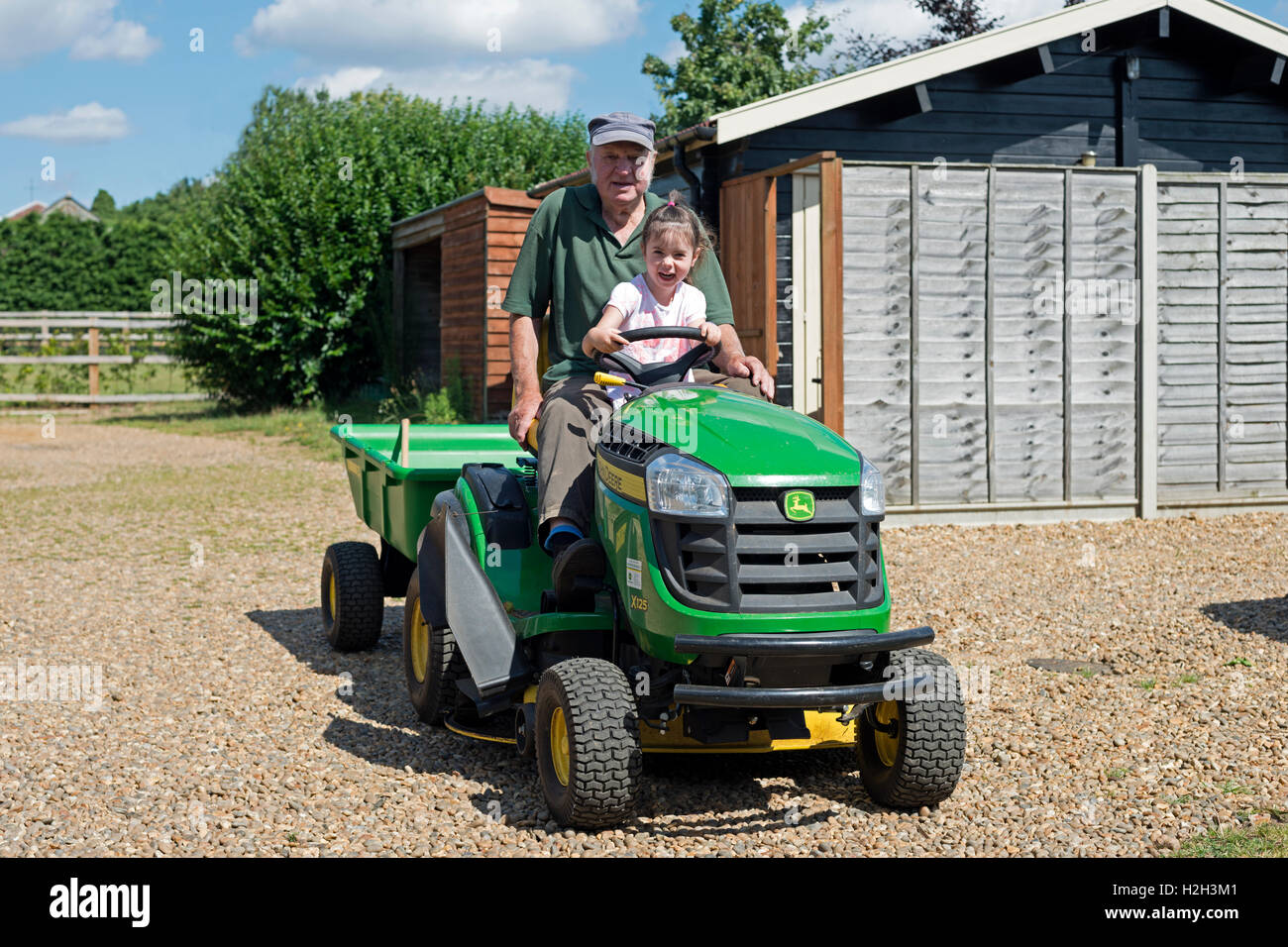 Großvater mit Enkelin fahren ein John Deere X 125 Rasenmäher Stockfoto