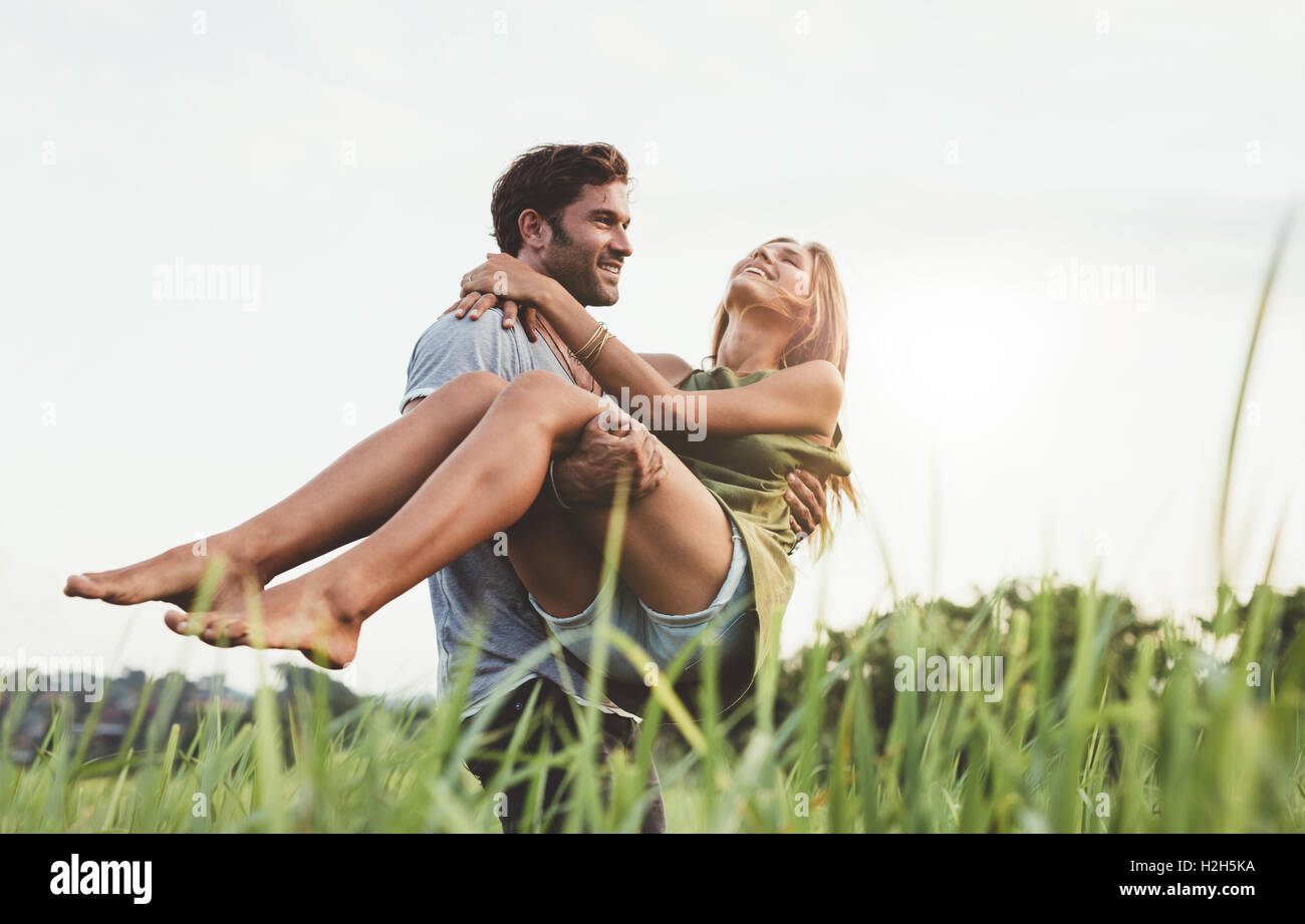 Junger Mann mit seiner Freundin durch eine Wiese. Paar im Urlaub in der Natur Spaß. Stockfoto