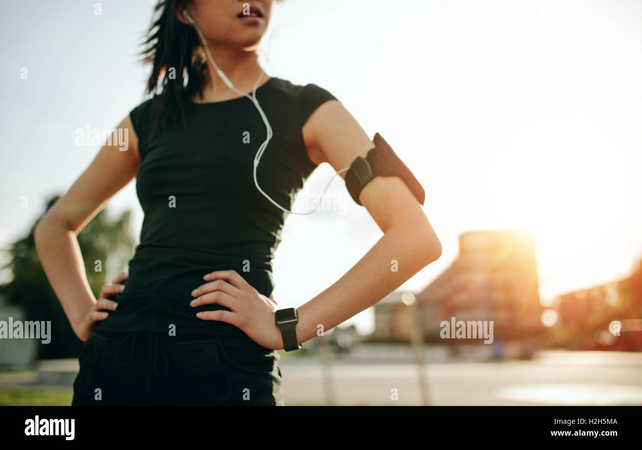 Abgeschnittene Aufnahme einer jungen Frau, die beim Morgenrennen eine Pause macht. Fitness-Frau mit Armband und Ohrhörern, die draußen stehen Stockfoto