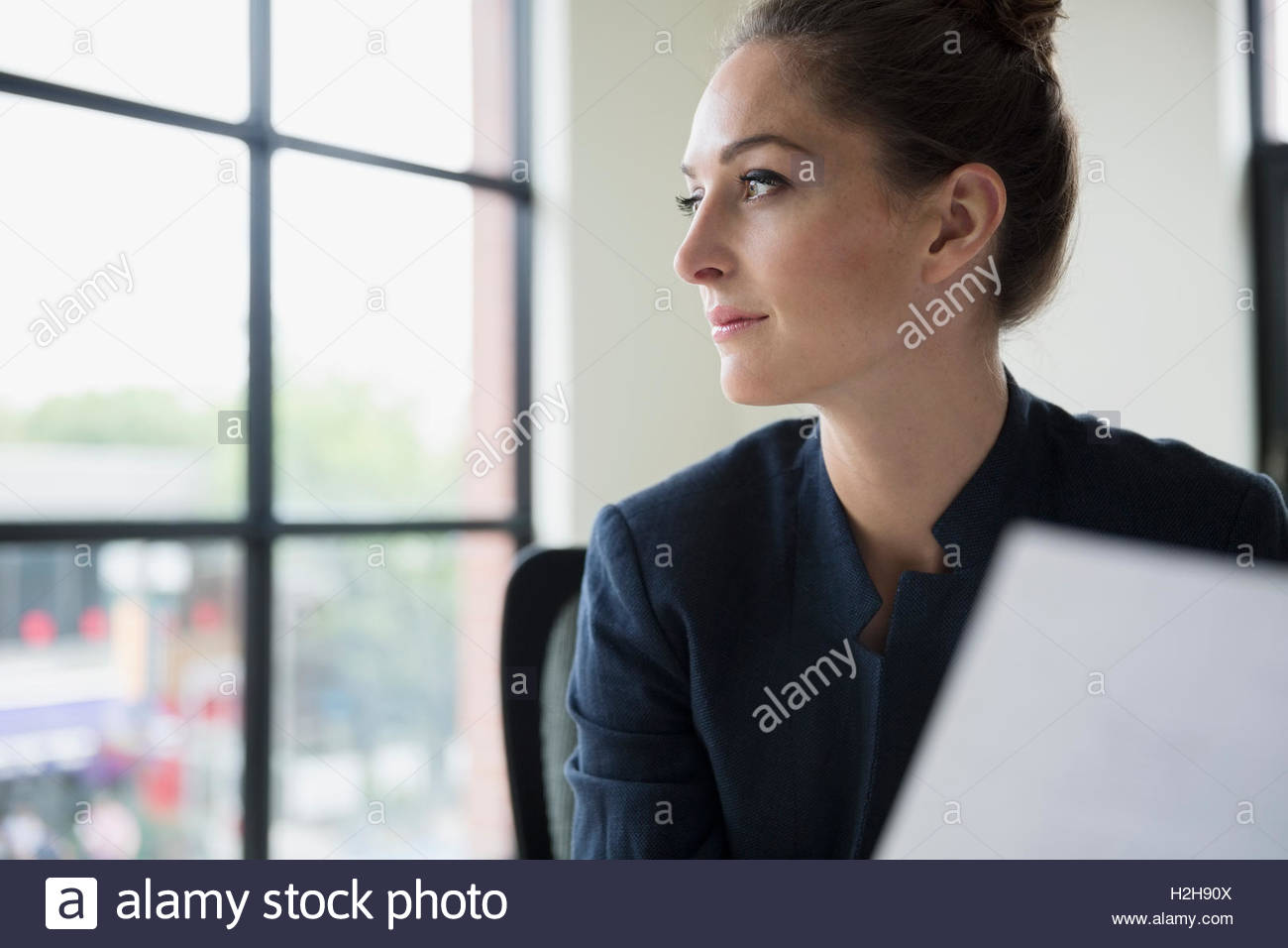 Nachdenklich Geschäftsfrau mit Papierkram Bürofenster mit Blick Stockfoto