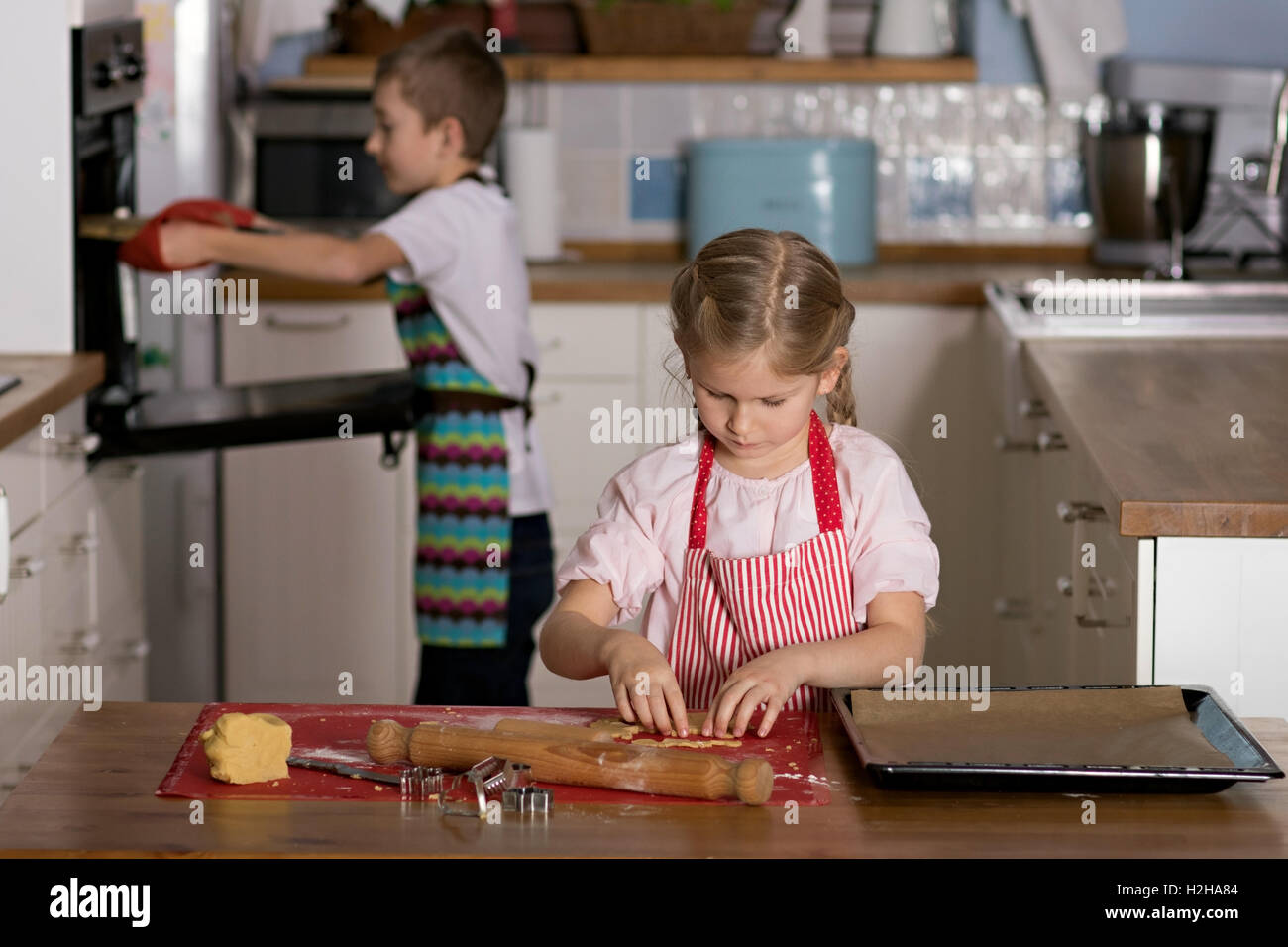 Junge unter einer Schale mit Keksen aus einem Ofen, während eine Mädchen Schnittformen aus in der Konditorei ist Stockfoto