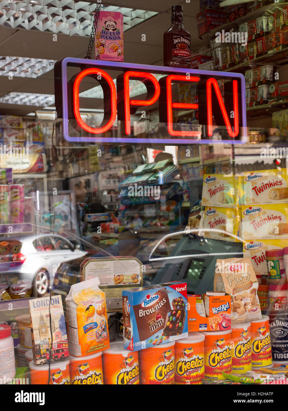 Schaufenster der Convenience-Store mit Schild "geöffnet" in Neonlicht. Verschiedene Produkte und Süßigkeiten im Angebot unten. Stockfoto