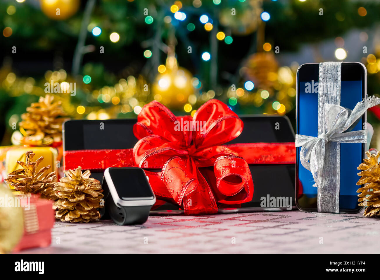 Tablet-pc, Smartphone und Smartwatch mit Geschenken und Dekorationen vor Weihnachtsbaum. Fokus auf Smartphone. Stockfoto