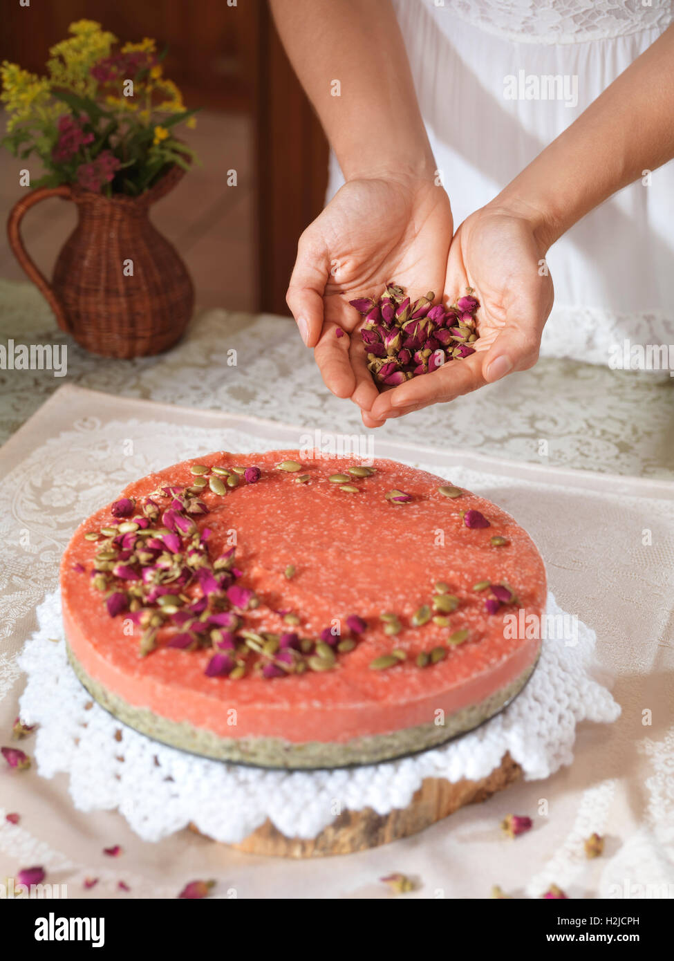 Nahaufnahme von Frau Hände einen hausgemachte Erdbeerkuchen mit Rosenknospen und Kürbiskerne zu Hause dekorieren Stockfoto