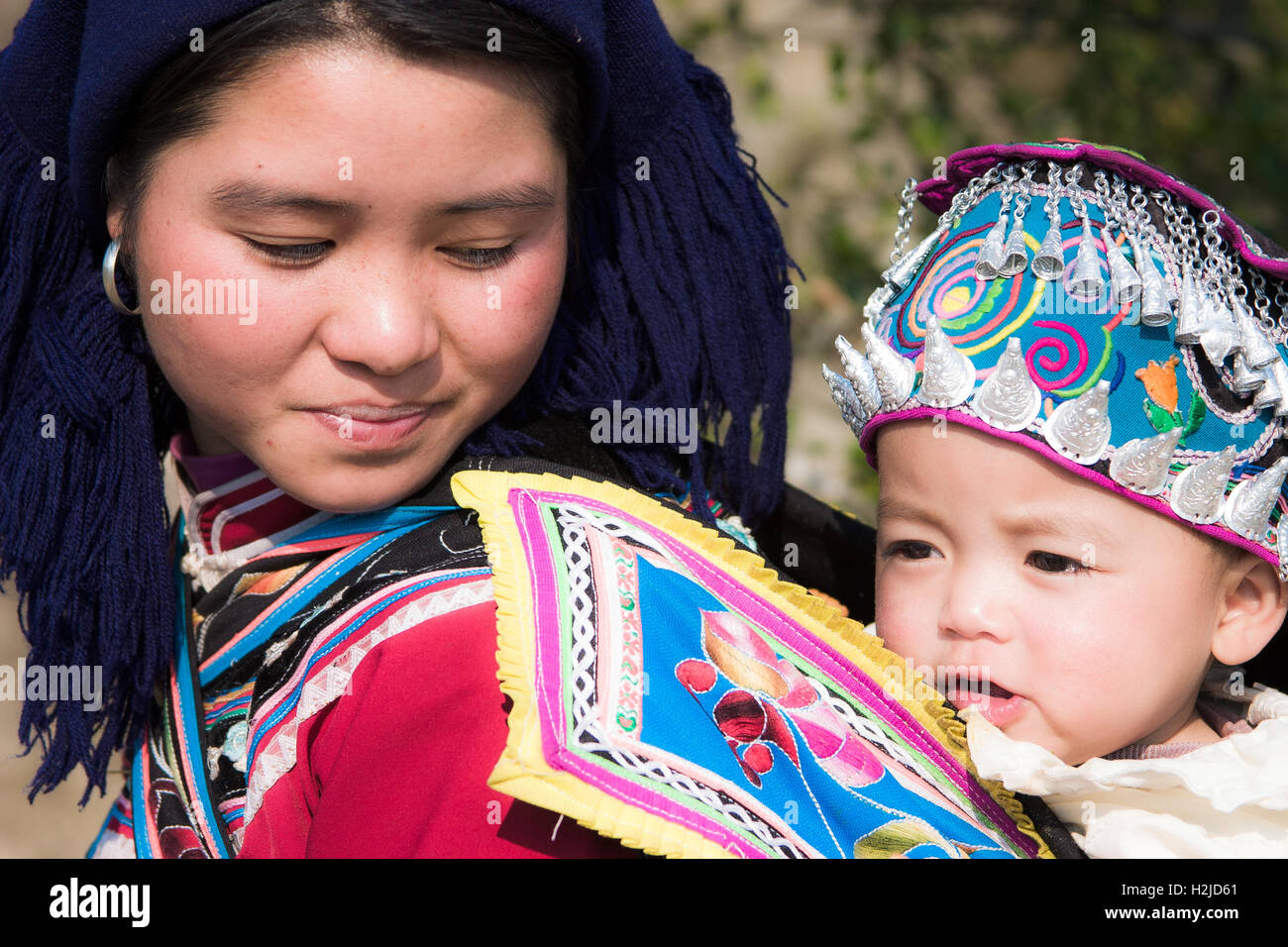 Eine junge Hani (ethnische Minderheit in China)-Mutter und Kind, durchgeführt in einem Rucksack tragen ihre traditionelle Kleidung. Stockfoto