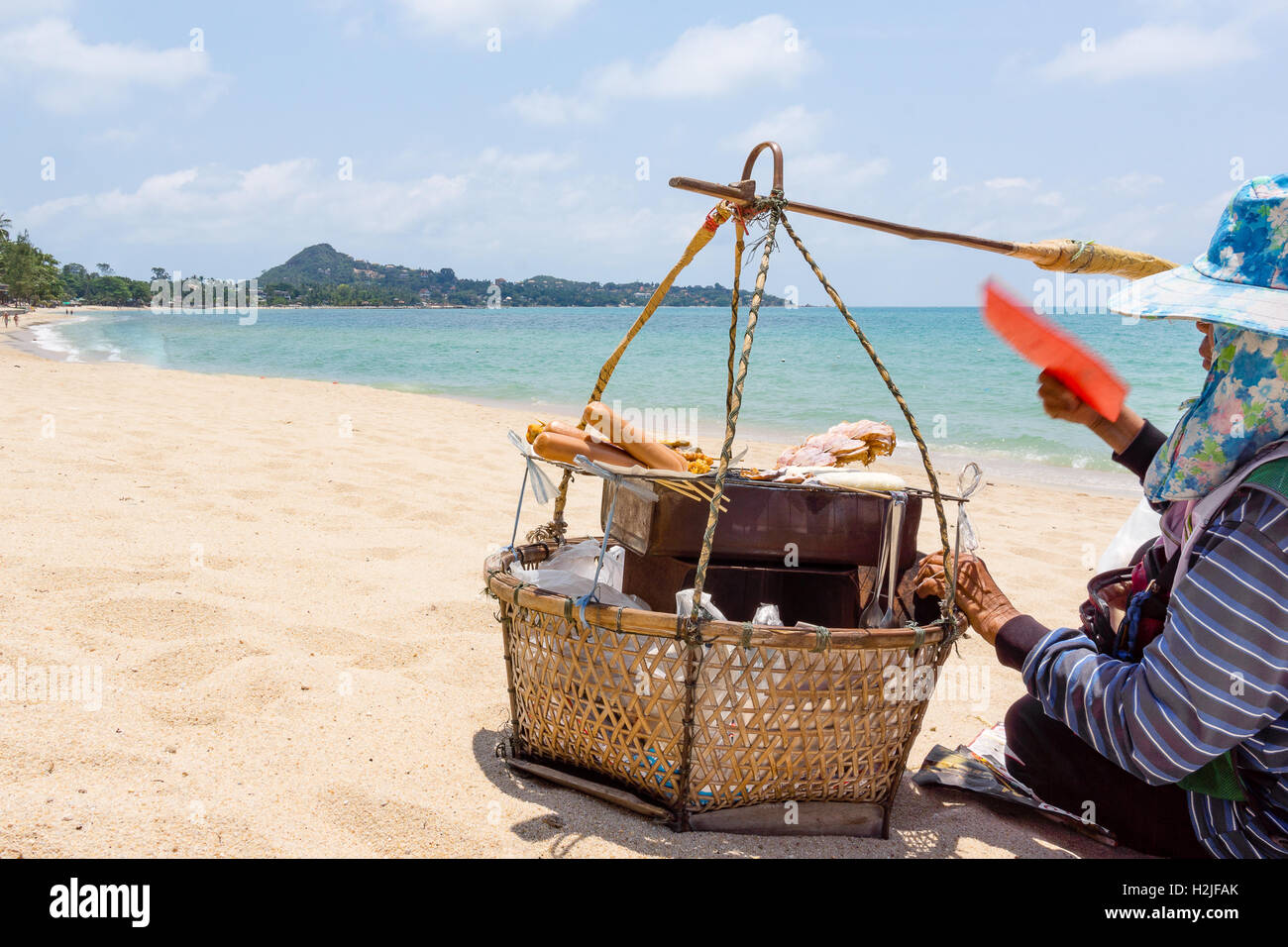 Thailändische Hersteller sitzen auf einem Sandstrand mit Ihrem Körbchen in der Nähe des Meeres grillen Würstchen für Touristen Stockfoto