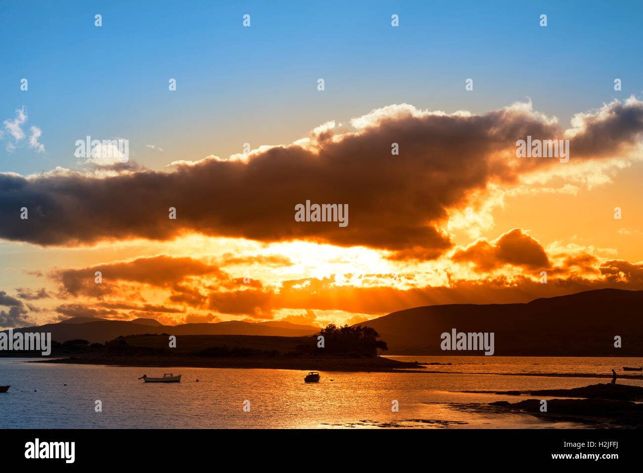 Boote in einer ruhigen Bucht mit Insel in der Nähe von Kenmare am Wilden Atlantik Way Irland mit einem roten Sonnenuntergang Stockfoto