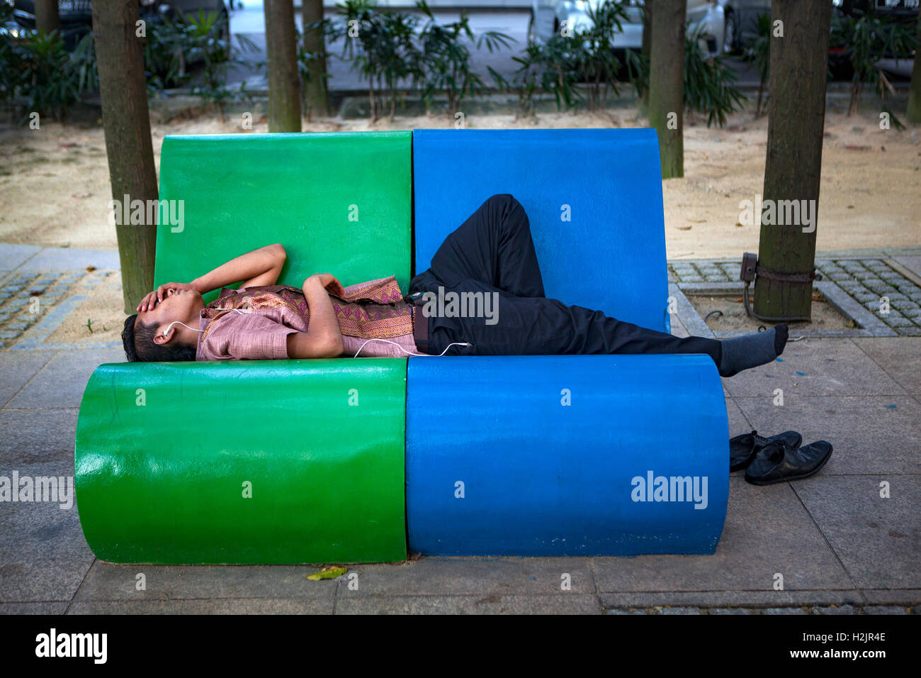 Ein junger malaysischer Mann nimmt ein Nickerchen auf einer Parkbank in Kuala Lumpur, Malaysia, Südost-Asien. Stockfoto