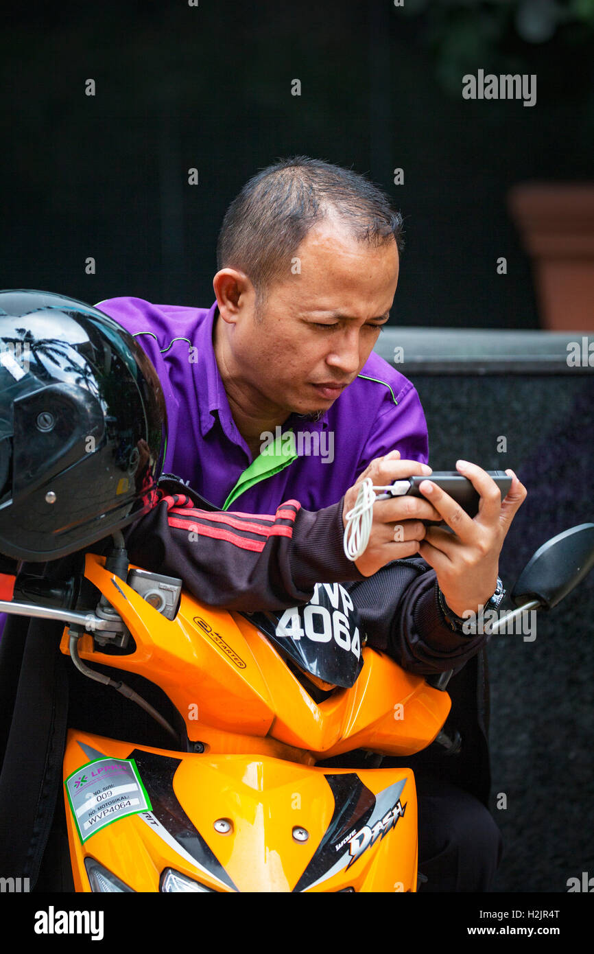 Ernsthafte suche Chinesische malaysischen Mann auf seine mit seinem Smartphone während des Verkehrsaufkommens in Kuala Lumpur, Malaysia Motorrad sitzen. Stockfoto