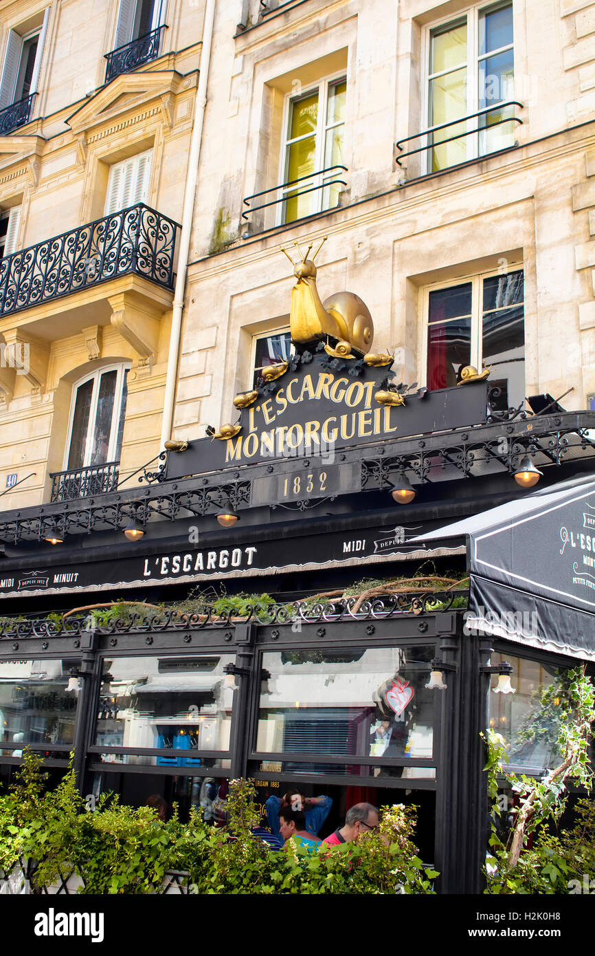 Menschen haben Mittagessen in einem traditionellen französischen Bistros in Paris. Restaurant Maskottchen goldene Schnecke ist auch in der Ansicht. Stockfoto