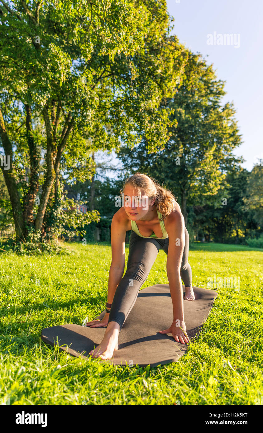 Vordere Splits, junge Frau in Sportkleidung dabei Training auf Matte im Park, München, Upper Bavaria, Bavaria, Germany Stockfoto