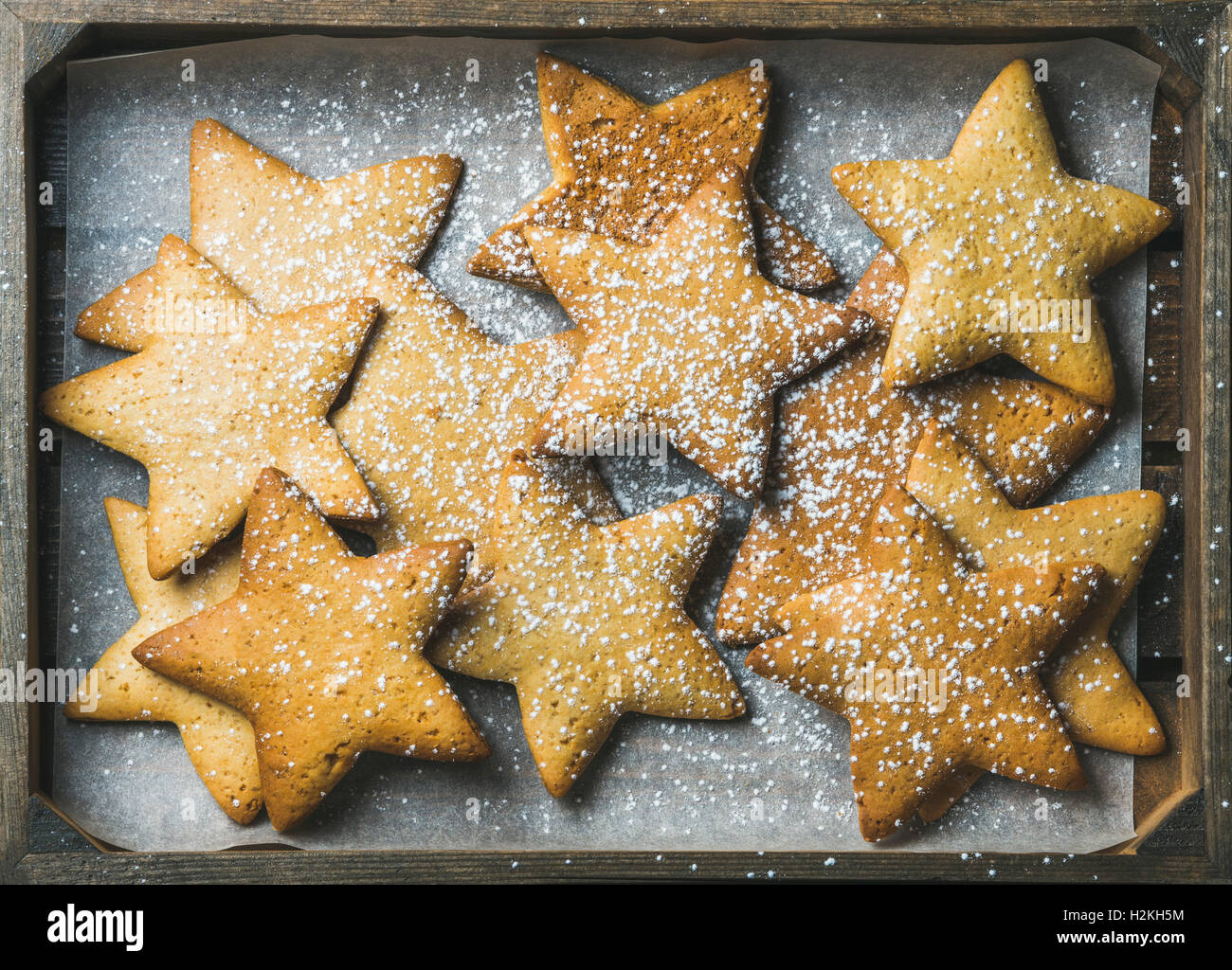 Süße Weihnachten Urlaub Lebkuchen in Form von Sternen mit Zuckerpuder auf Backpapier in rustikales Holztablett, Ansicht von oben, Stockfoto