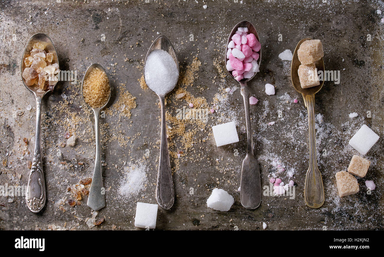 Verschiedene Vintage Löffel mit unterschiedlichsten Zucker weiß, braun, rosa Früchte granuliert, Würfel und Kristall über alte Textur Eisen backg Stockfoto