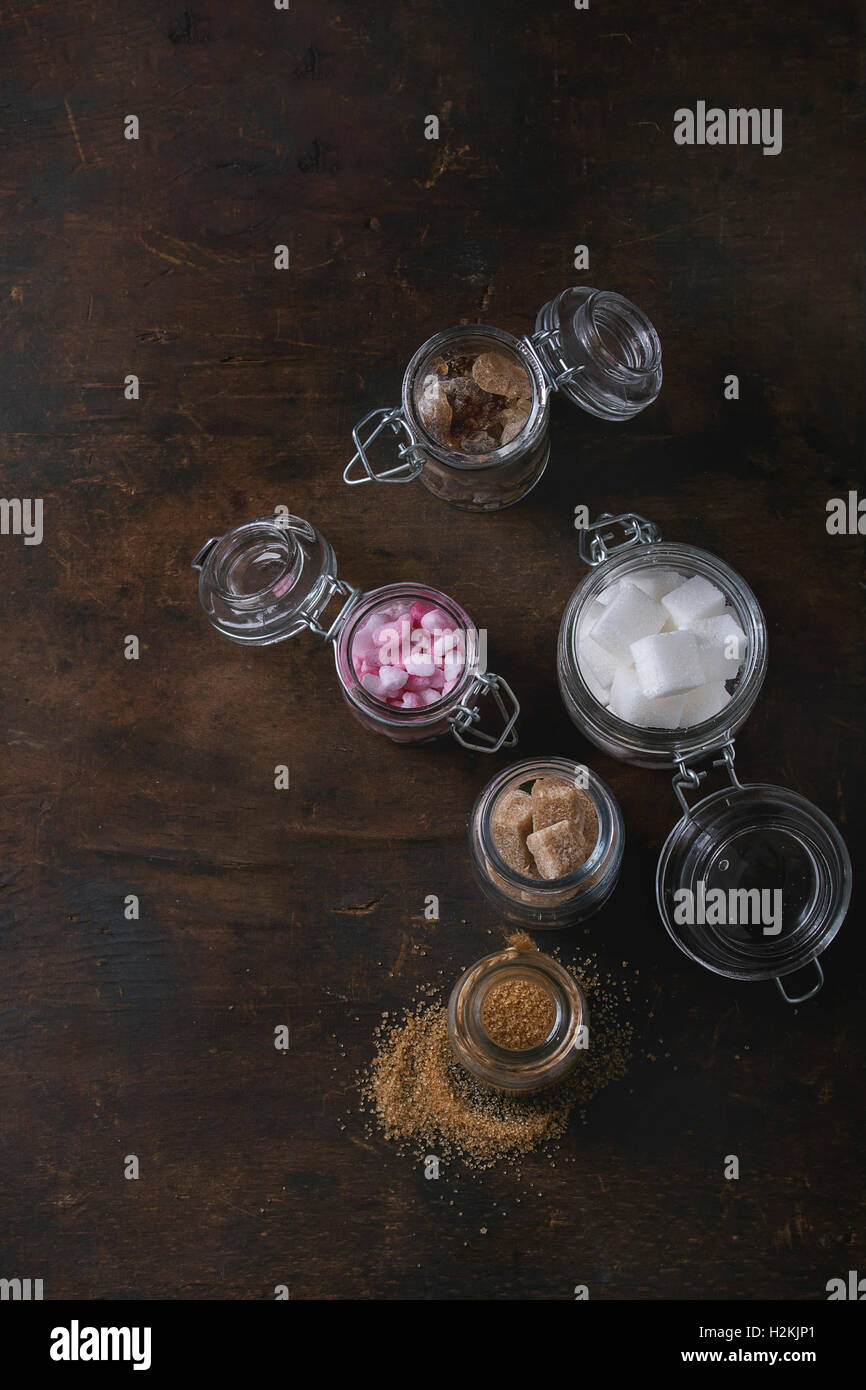 Verschiedenen Gläsern mit Vielzahl von Zucker weiß, braun, rosa Früchte granuliert, Würfel und Kristall über alte Holz dunkel. Stockfoto
