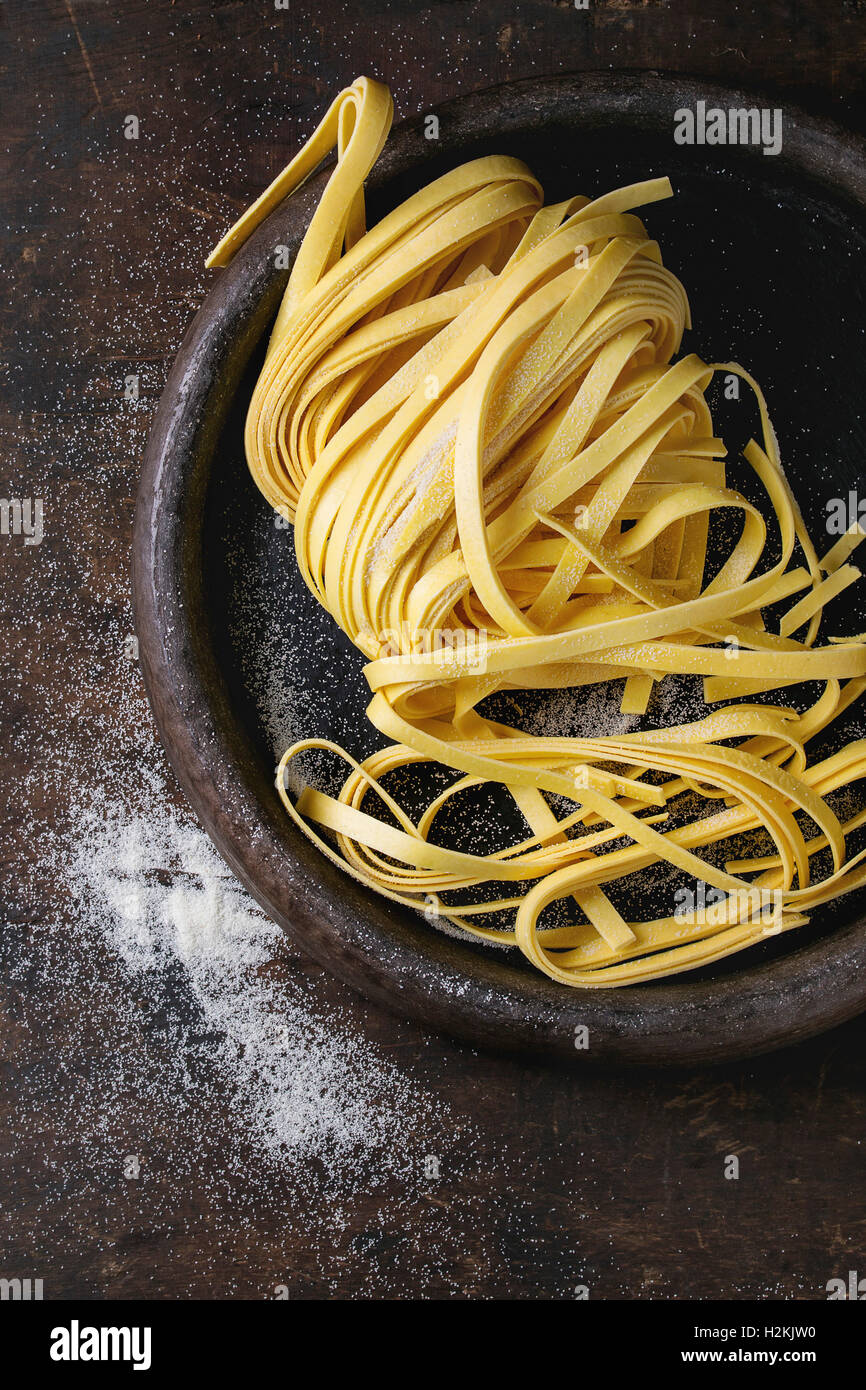 Rohe hausgemachte italienische Teigwaren Tagliatelle mit Mehl in alten Ton Fach über dunklem Holz. Draufsicht mit Platz für Stockfoto