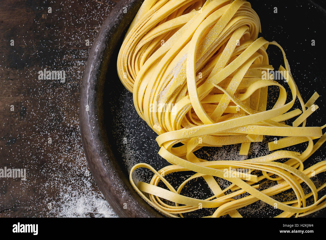 Rohe hausgemachte italienische Teigwaren Tagliatelle mit Mehl in alten Ton Fach über dunklem Holz. Draufsicht mit Platz für Stockfoto